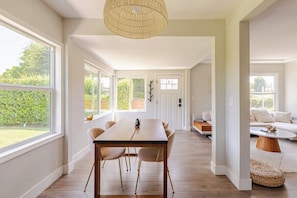 A spacious room with a dining table, chairs, and a large window. - The Cozy California Bungalow (Inglewood)
