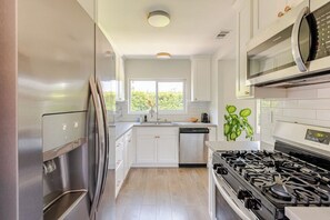 A kitchen with white cabinets, stainless steel appliances, a window, and a plant. - The Cozy California Bungalow (Inglewood)