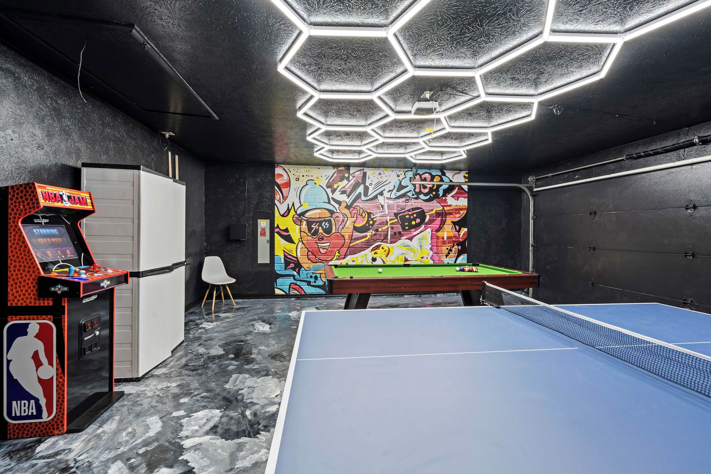 Una stanza con tavolo da biliardo, videogioco a basket arcade e una parete decorata con graffiti colorati.