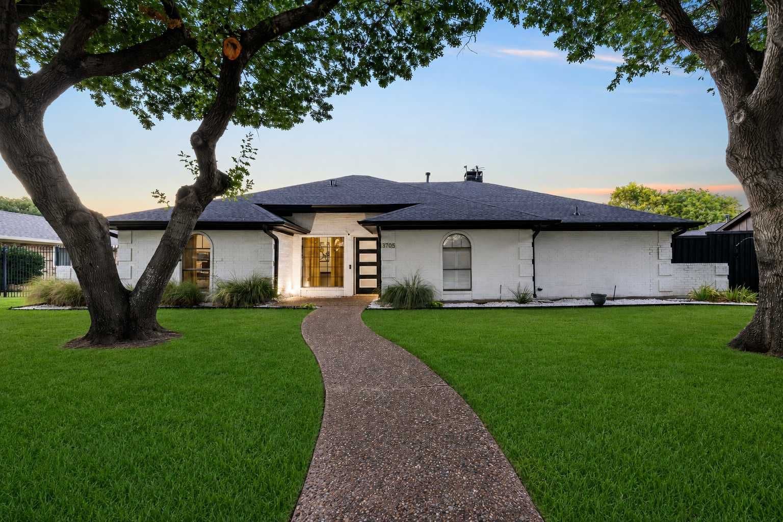 A single-story house with a paved driveway leading to a front door, surrounded by well-maintained grass and trees.