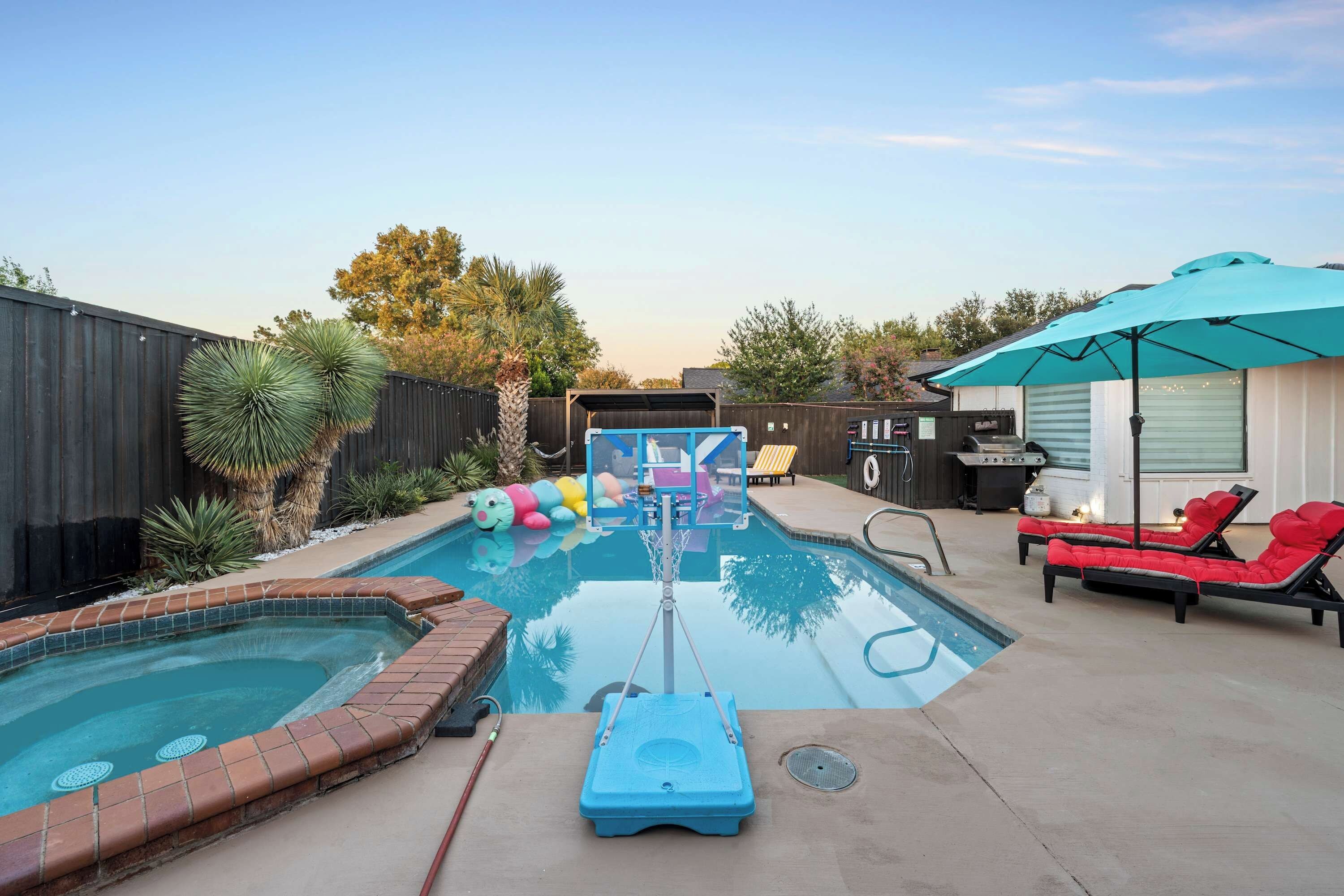 A backyard with a swimming pool, a hot tub, lounge chairs, and a barbecue area.