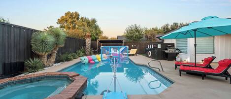 A backyard with a swimming pool, a hot tub, lounge chairs, and a barbecue area.
