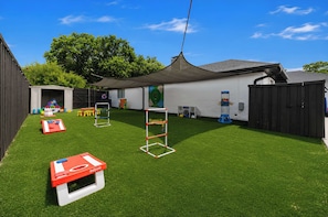 Ein Garten mit Kunstgrasanlage, einer Kletterkonstruktion, einem kleinen Spielhäuschen und einem eingezäunten Bereich.