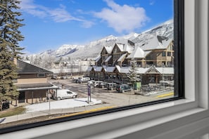 A town with buildings, a parking lot, and snow-covered mountains in the background. - The Canmore Mountain View Retreat with Heated Pool & Hot Tub (Canmore)