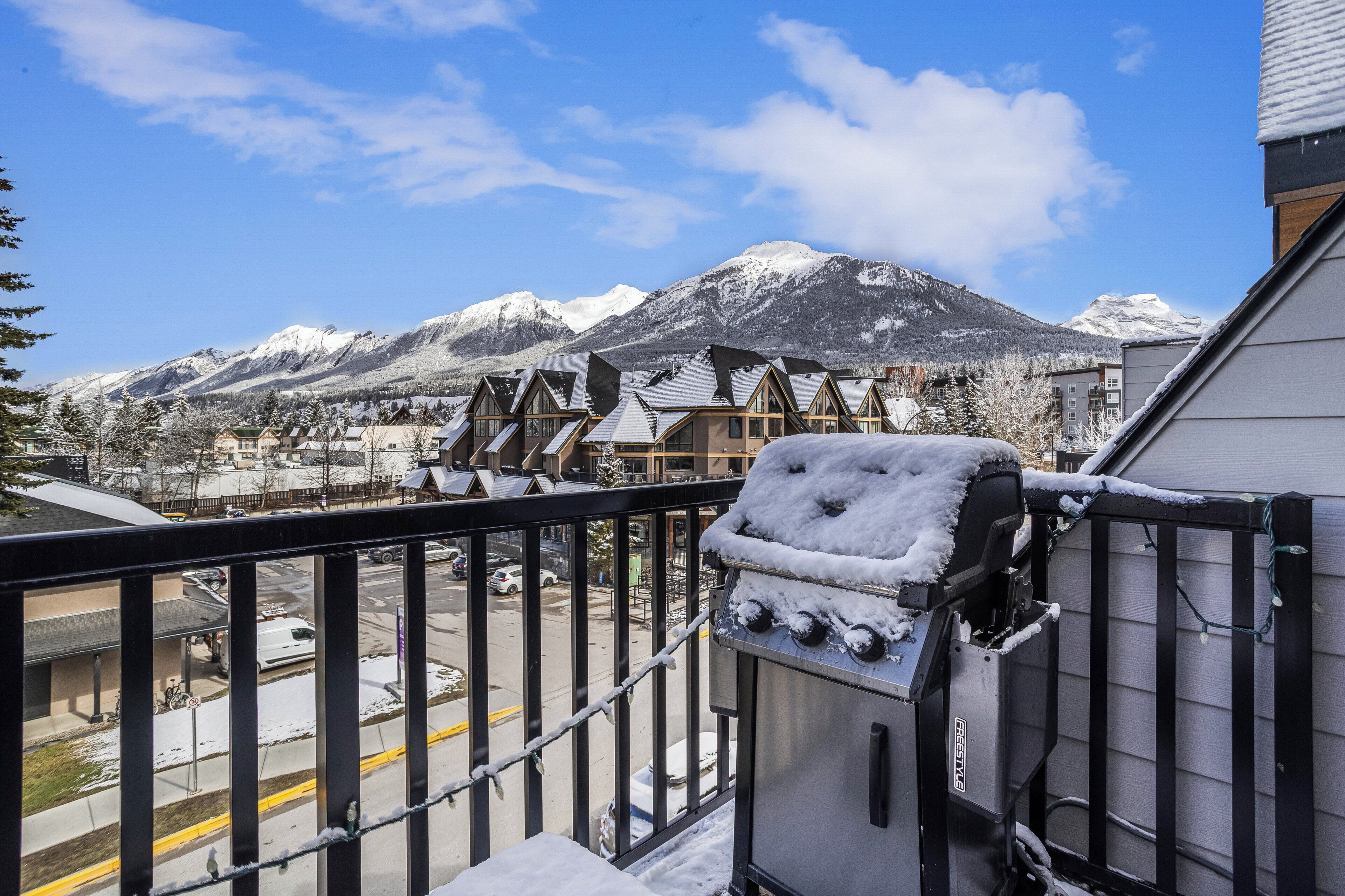 En balkon med sne, der kigger ud over en by med huse og et bjerglandskab i baggrunden.