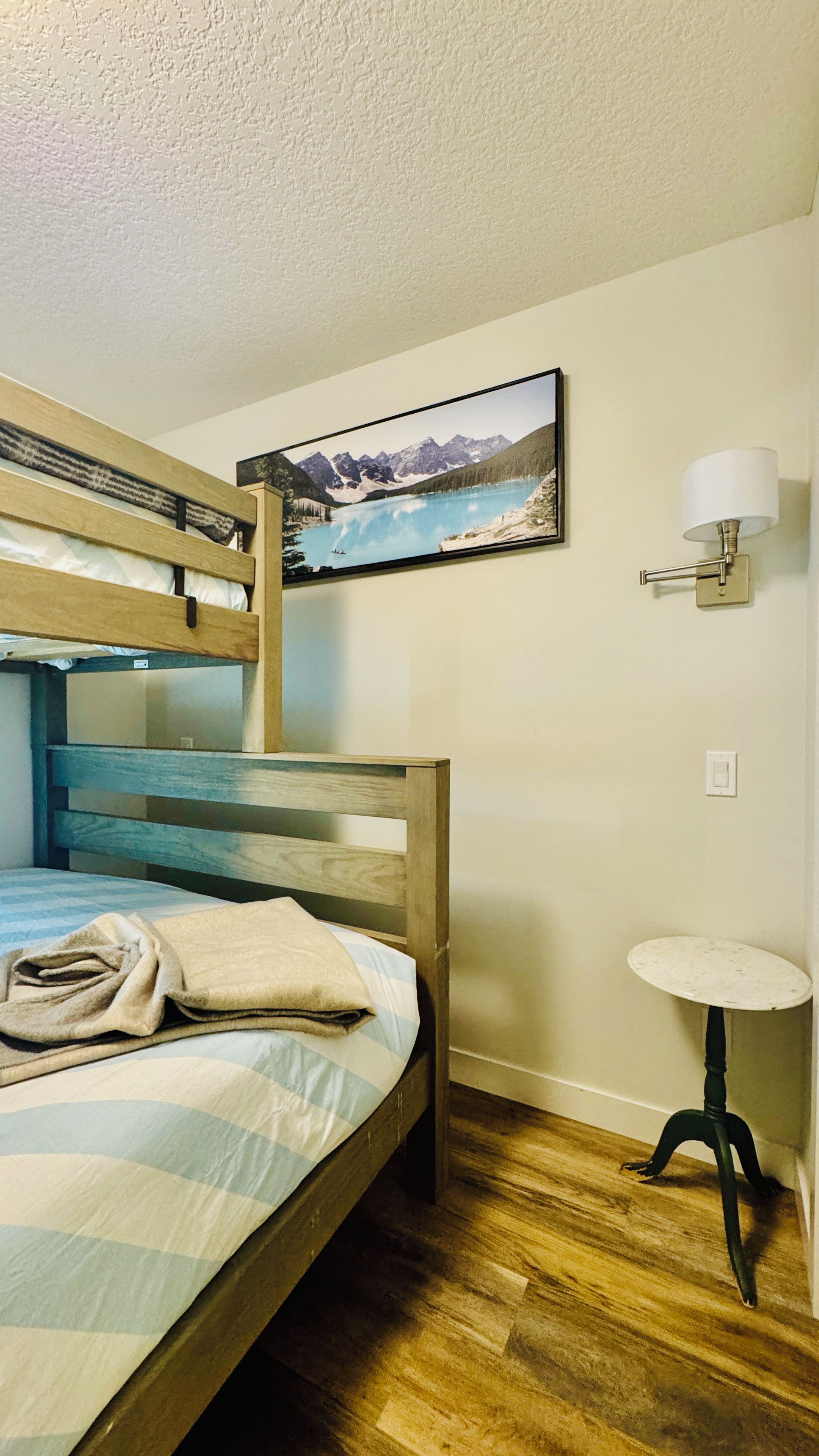 A bunk bed with a view of a mountain lake, a small table with a lamp, and a wall-mounted light fixture.