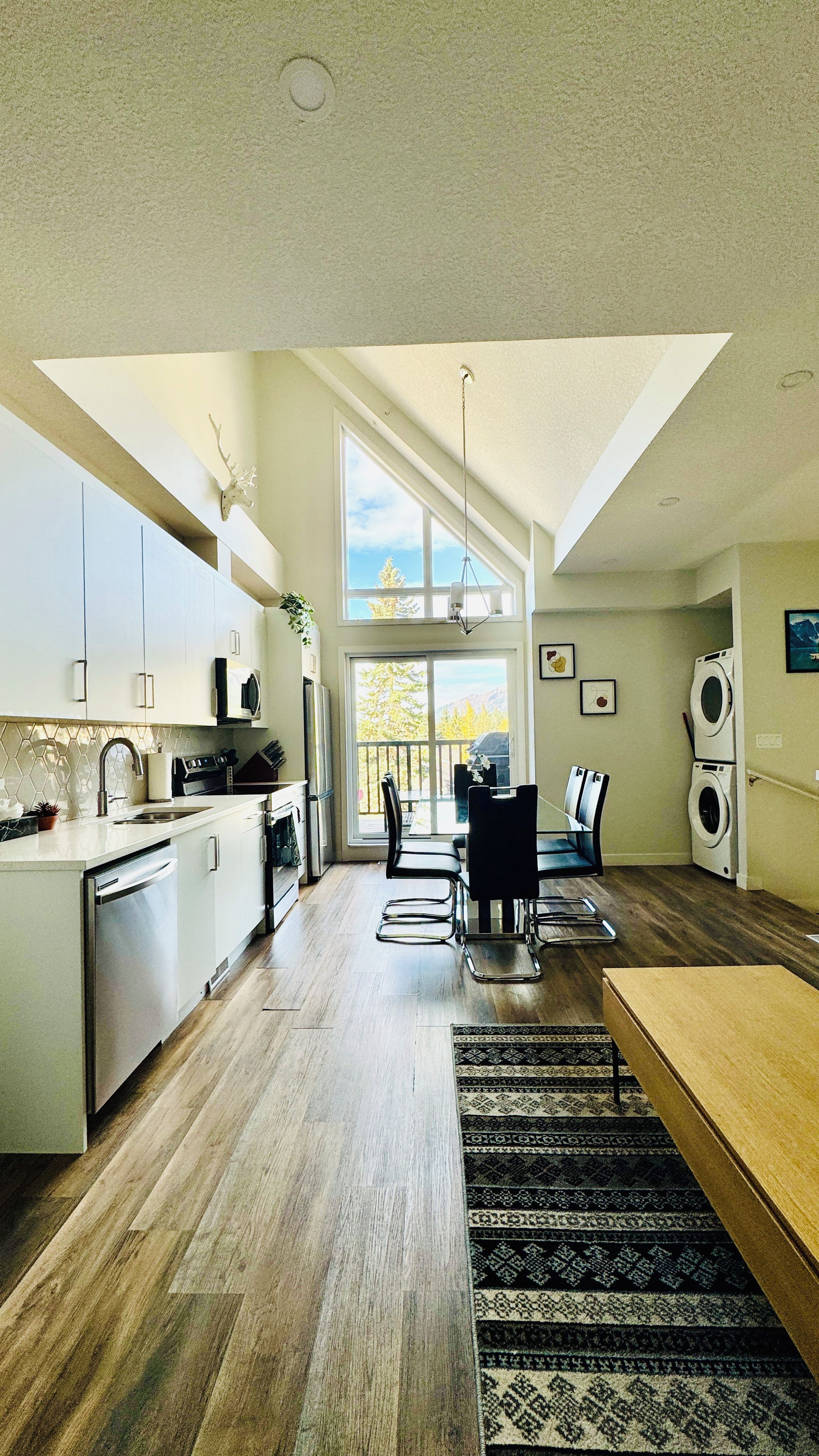 A modern kitchen with a dining area, large windows, and a view of the outdoors.