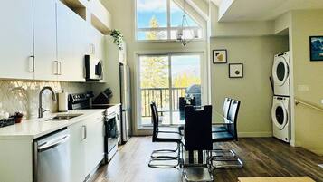 A modern kitchen with a dining area, large windows, and a view of the outdoors.