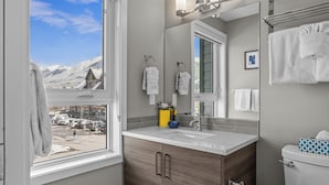 Une salle de bain avec une fenêtre donnant sur un paysage montagneux enneigé, un lavabo avec un miroir et des toilettes.