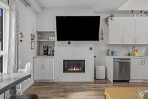 A modern kitchen with a built-in fireplace, a flat-screen TV, and a coffee machine. - The Canmore Mountain View Retreat with Heated Pool & Hot Tub (Canmore)