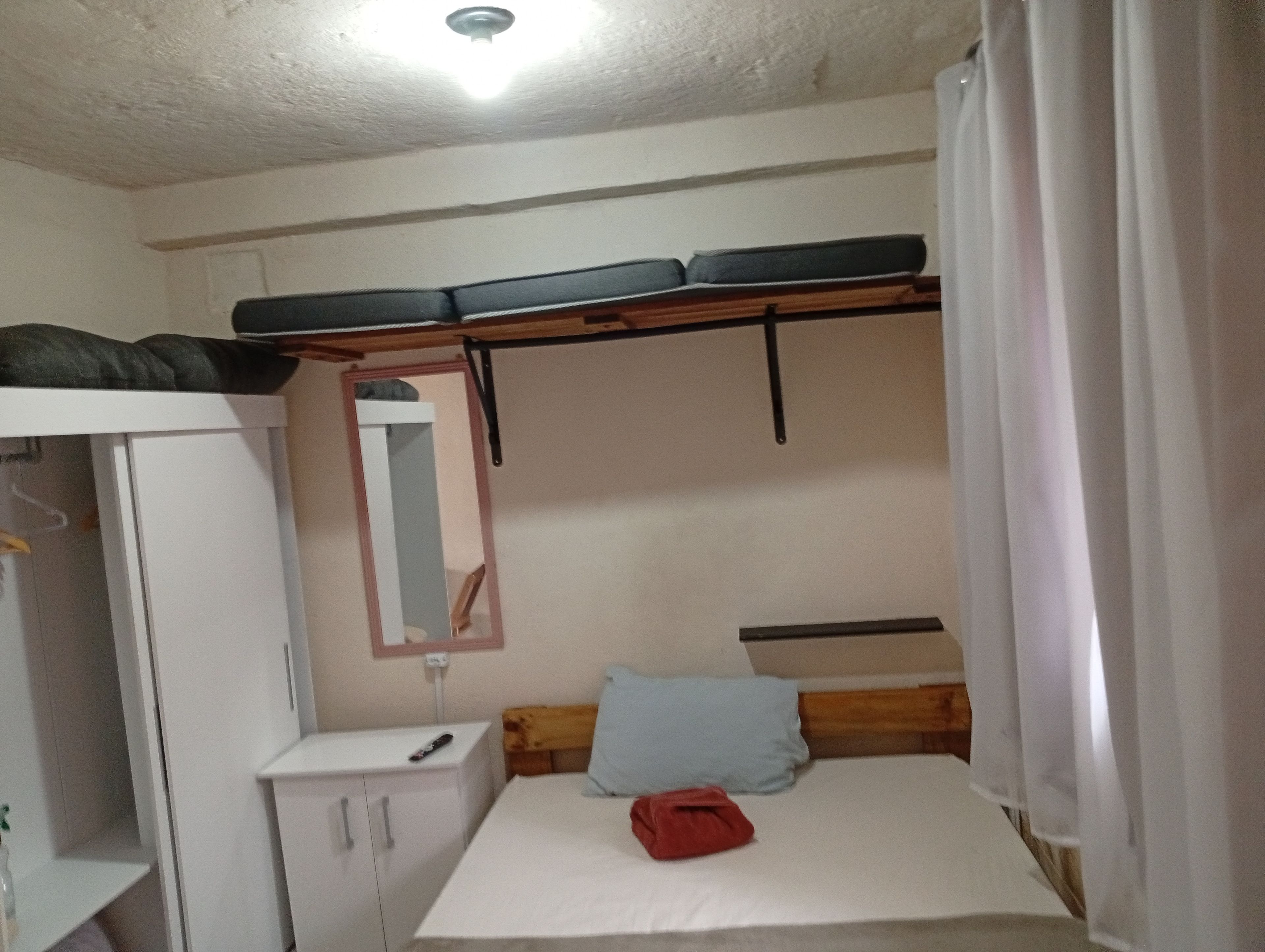 A small, compact room with a bunk bed, a bedside table, a mirror, and a wardrobe.