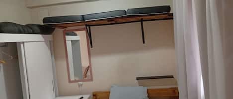 A small, compact room with a bunk bed, a bedside table, a mirror, and a wardrobe.