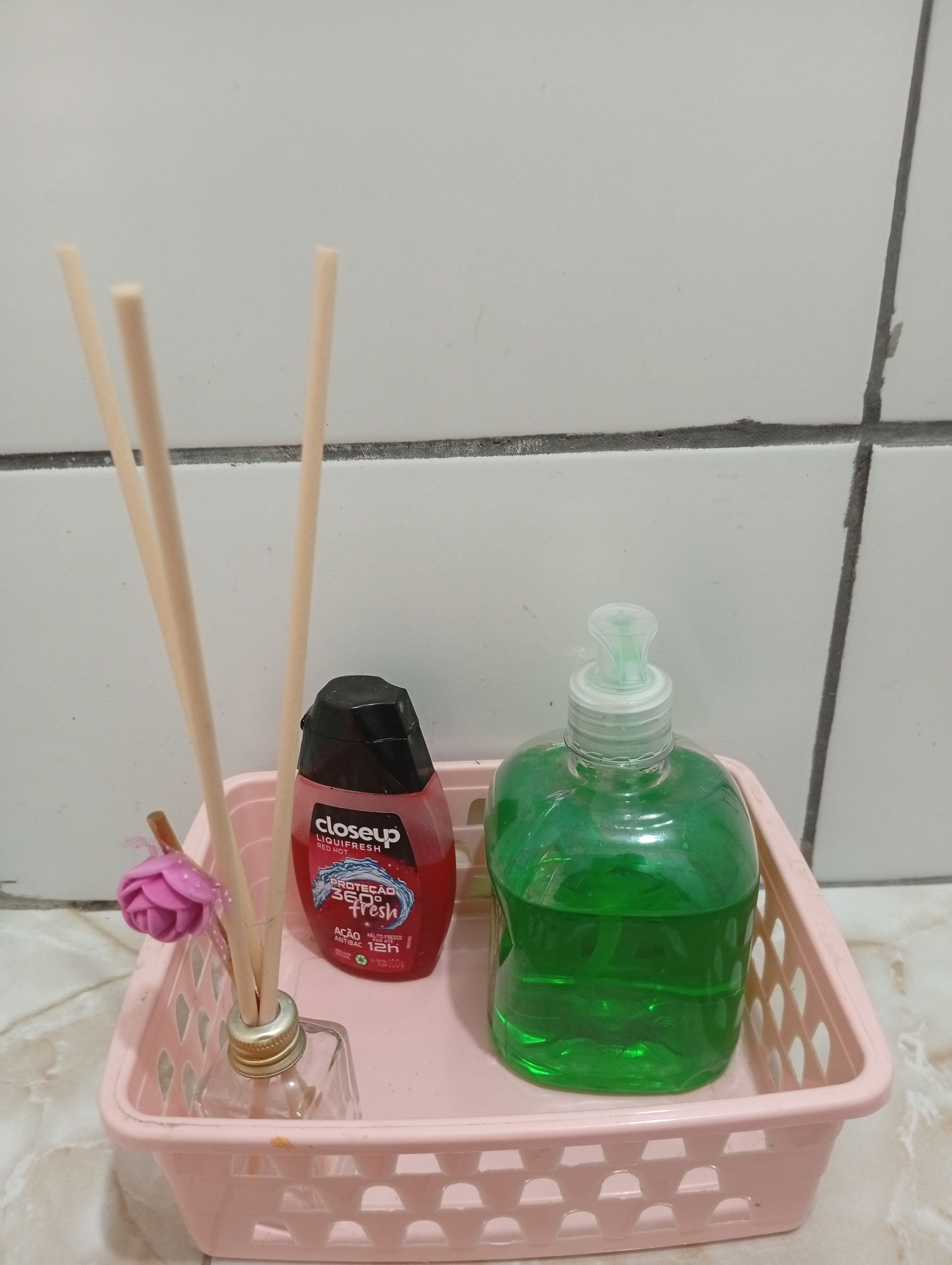 A pink basket containing a bottle of Clorox liquid fresh, a green bottle of dish soap, and two wooden sticks.