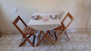 Ein kleiner Esstisch mit einer blumigen Tischdecke, zwei Holzstühle und ein Paar gestreifte Flip-Flops darauf.