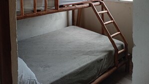 Ein Stockbett mit Holzleiter, Deckenventilator und Fenster mit Metallgitter.
