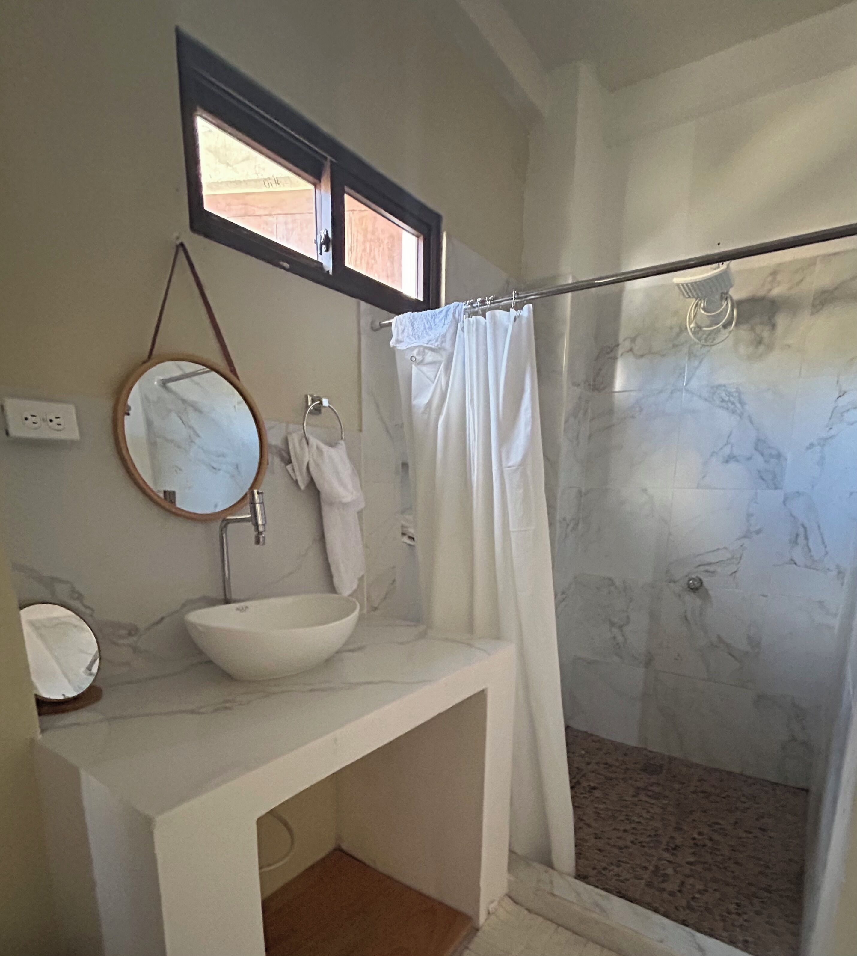 A bathroom with a white sink, a round mirror, a towel rack, and a shower with a glass door.