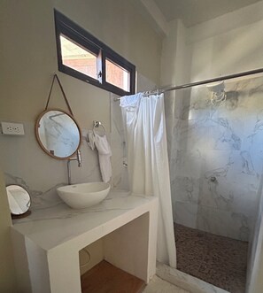 A bathroom with a white sink, a round mirror, a towel rack, and a shower with a glass door.
