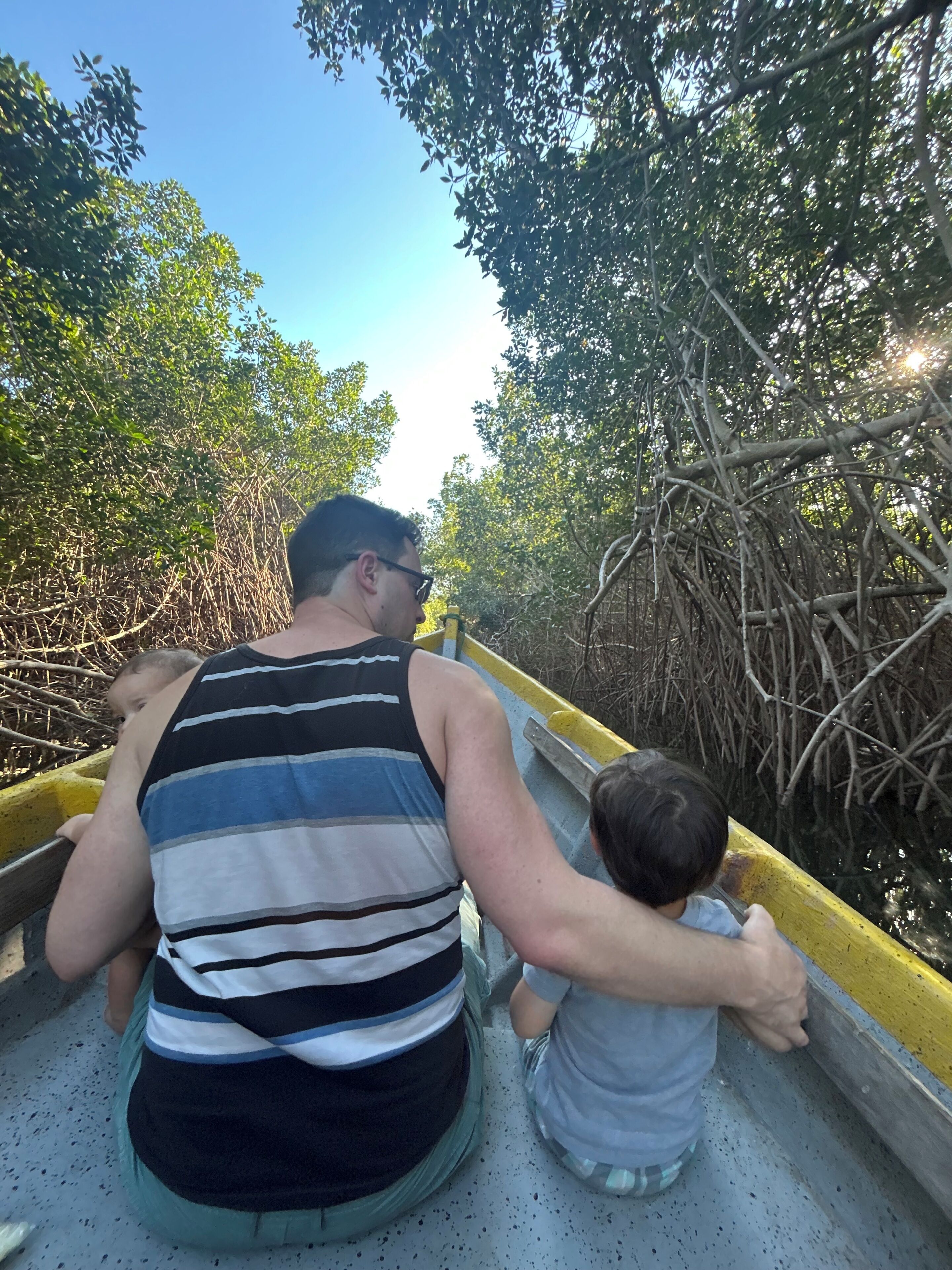 A man and a child in a boat on a waterway surrounded by dense mangrove trees.