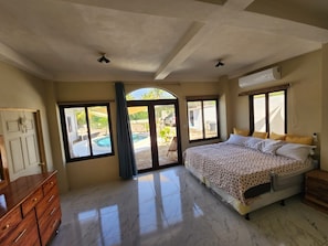 Una camera da letto con un letto, una cassettiera, una finestra e vista su una piscina.