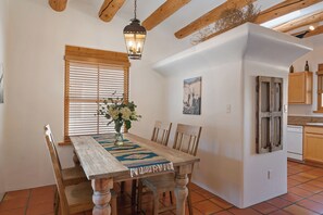 Un comedor con mesa de madera, sillas, un jarrón con flores y una lámpara colgante.