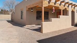 A building with a flat facade, a covered porch with wooden beams, and a small entrance door. - Ideal location, Kiva Fireplace, 2 Bedroom, 2 Bathroom with parking! (Santa Fe)