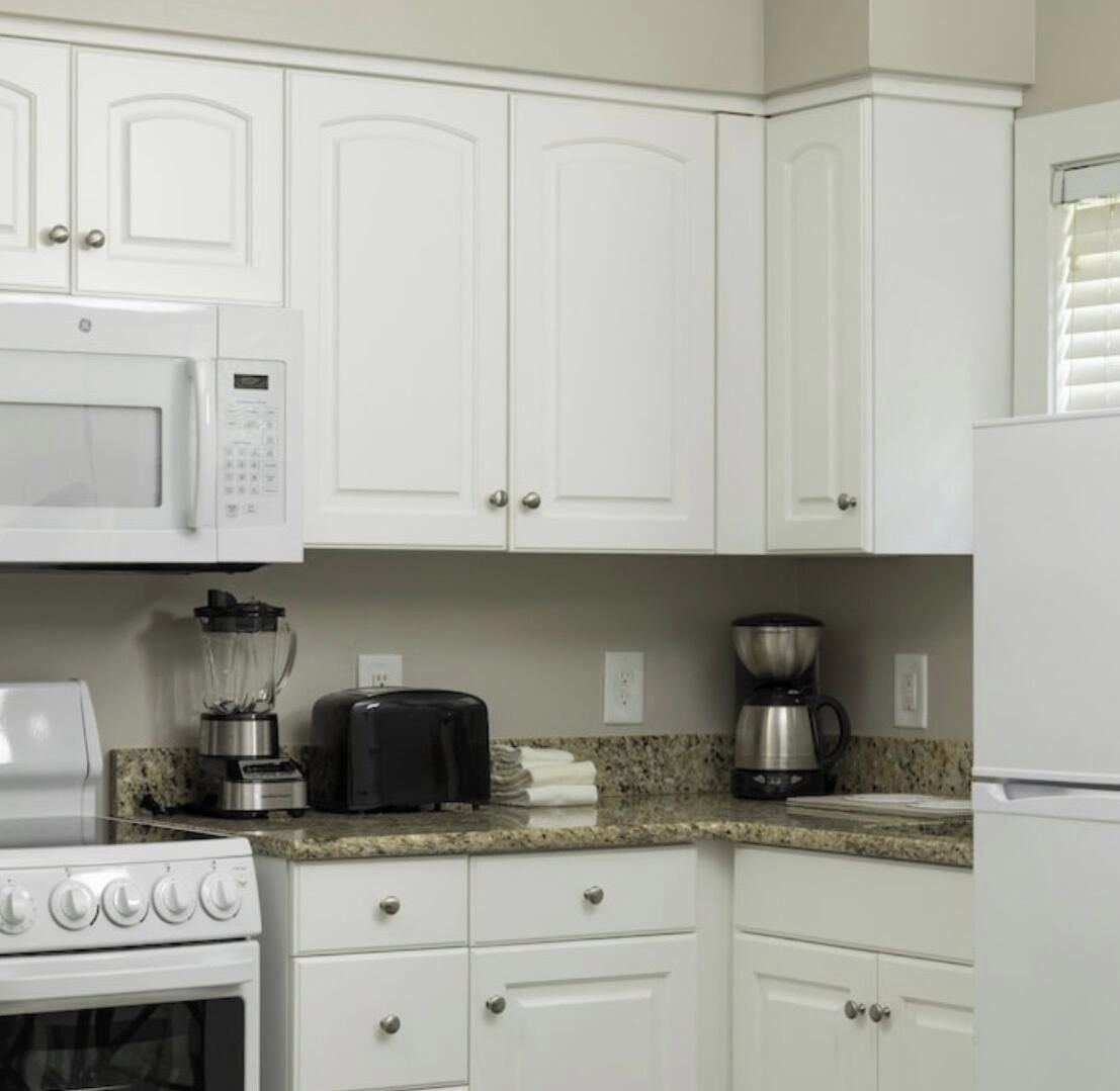 A kitchen with white cabinets, a microwave, a toaster, a blender, a coffee maker, and a stove.