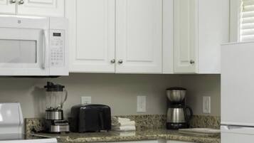 A kitchen with white cabinets, a microwave, a toaster, a blender, a coffee maker, and a stove.