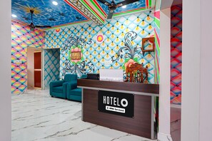 A hotel reception area with a colorful wall design, a reception desk, and a blue sofa. - Deluxe Jyoti Inn (Ali)