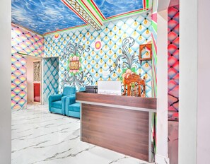 Ein Zimmer mit einem gemusterten Decken, einem blauen Sofa, einem hölzernen Empfangstresen und einer Wandverzierung.