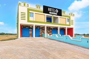 A hotel with a prominent sign, multiple garage doors, and a flat roof. - Deluxe Jyoti Inn (Ali)
