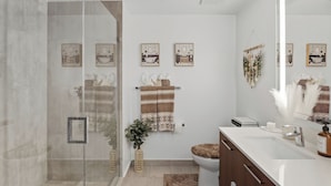Un baño moderno con cabina de ducha de vidrio, lavamanos blanco, espejo y retrete.
