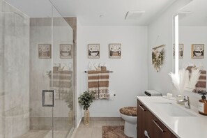 Een moderne badkamer met een douchecabine van glas, een witte wastafel, een spiegel en een toilet.
