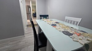 Ein Essbereich mit einem Tisch für vier Personen, Stühlen und einer Küche im Hintergrund.