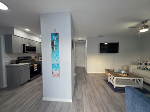 A modern kitchen with grey cabinets and stainless steel appliances, a living area with a white sofa and a coffee table, and a hallway with a 'WELCOME' sign. - Seaside Village 2. 3 minutes to Anna Maria Island. Boat, Jetsky and Rv parking (Bradenton)