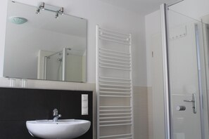 Casa de banho com lavatório branco, espelho e cabine de duche em vidro.