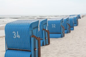 Fileiras de cadeiras de praia com números, dispostas na areia, com um píer ao fundo.