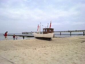 A boat on a sandy beach with a pier in the background. - Romantic vacation rental in a thatched-roof house (upper floor) with a large, child-friendly garden (Koserow)