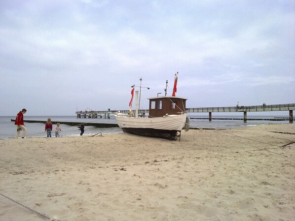 A boat on a sandy beach with a pier in the background.