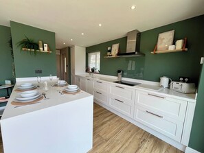 A modern kitchen with white cabinetry, a central island, and a green accent wall. - 2bed Modern Home Garden Off Road Parking (Bath and North East Somerset)