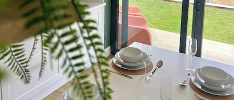 A dining area with a table set for four, a glass door leading to a garden, and a view of a residential area.