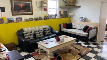 Una habitación con piso a cuadros, un sofá de cuero negro, un sofá estampado, una pequeña mesa con objetos y un animal montado.