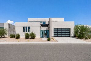 A modern building with a garage door, a covered entrance, and a landscaped area with small shrubs. - Pura Vista Palm Springs - 3BR + Private Pool + Casita + Mountain Views (Palm Springs)