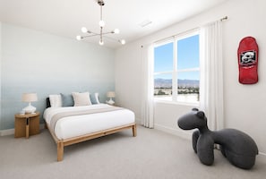 Ein Schlafzimmer mit Bett, Nachttischen, einer besonderen Deckenleuchte, einem großen Fenster mit Blick auf Windkraftanlagen und einer Skateboard-Dekoration an der Wand.