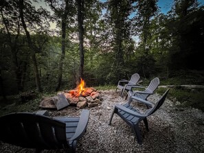A campsite with a fire pit surrounded by Adirondack chairs. - Modern Rustic Black Oak Tower – Treetop Views (Stanton)