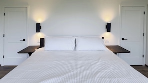 A bed with white bedding, two bedside tables, and wall-mounted lights. - Modern Rustic Black Oak Tower – Treetop Views (Stanton)