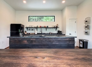 A modern kitchen with a large island, built-in appliances, and a window above the sink. - Modern Rustic Black Oak Tower – Treetop Views (Stanton)