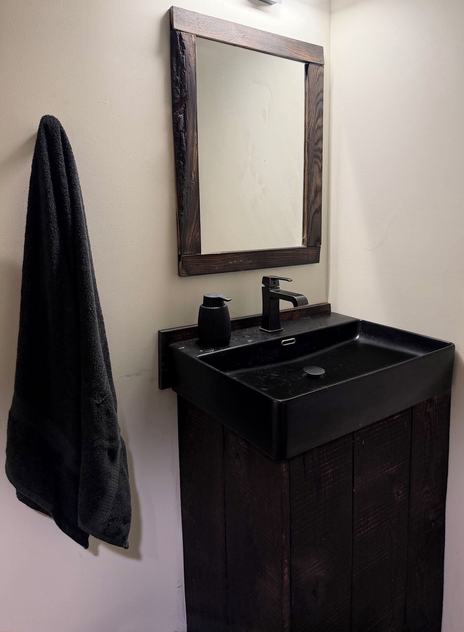 A bathroom with a black sink, a mirror with a wooden frame, and a towel hanging on the wall.