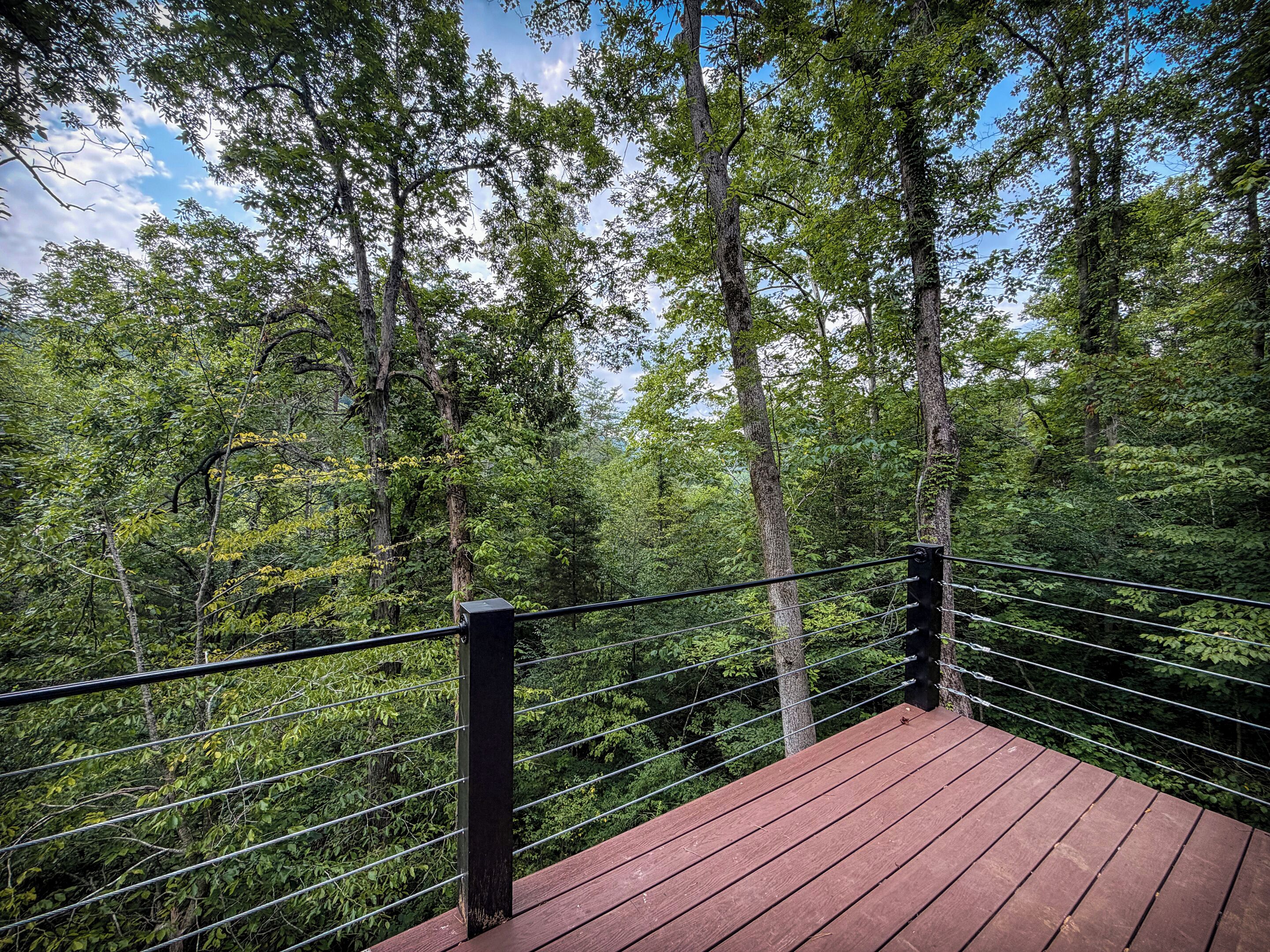 A wooden deck with a metal railing overlooking a forested area.