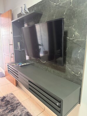 A flat-screen TV mounted on a wall with a marble-like texture. - Charming 2-bedroom house in serene Foz do Iguaçu with AC (Foz do Iguaçu)