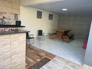 A kitchen with a countertop and chairs, a dining table with benches, and a tiled floor. - Charming 2-bedroom house in serene Foz do Iguaçu with AC (Foz do Iguaçu)